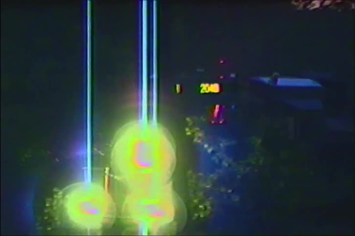 Eerie vintage footage of glowing lights on a pole at night, slowly zooming into a distant digital scoreboard