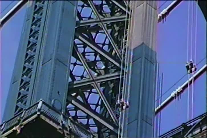 Vintage footage slowly zooms in on the intricate steel architecture of a Manhattan Bridge tower against a clear blue sky