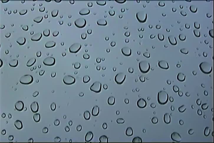 A close-up, static shot of raindrops resting on a glass surface against a flat, grey, overcast sky