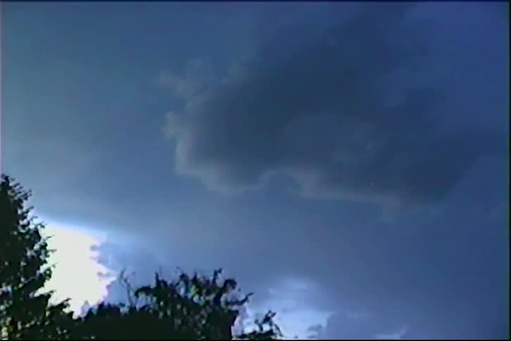 Flashes of lightning illuminate dark, ominous storm clouds in vintage VHS footage