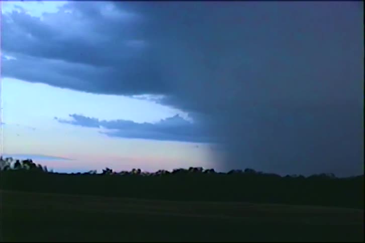 Vintage footage shows a dark thunderstorm with lightning flashes moving across the sky at dusk