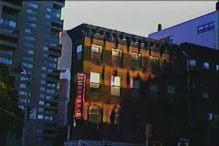 Vintage VHS footage shows a classic brownstone apartment building glowing in the afternoon sun in a modern city