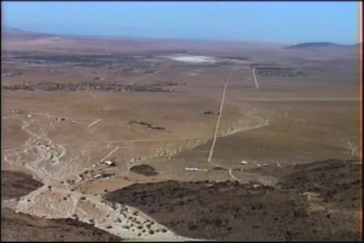 A slow zoom from a high-angle perspective reveals a vast and arid desert valley with a dark lava field, captured on vintage VHS