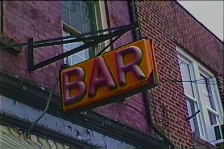 A low-angle shot slowly zooms out from a weathered 'BAR' sign hanging from a brick building