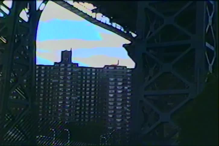 Vintage VHS footage zooms in on a New York City apartment building from underneath the massive steel structure of a bridge