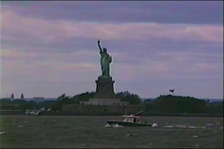 A small boat cruises past the iconic Statue of Liberty in New York City on a cloudy day, captured in vintage VHS footage