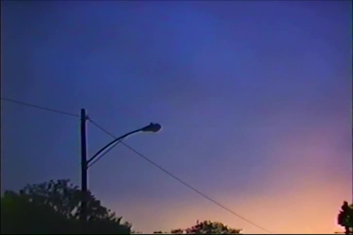A street lamp is silhouetted against a colorful gradient sky at dusk in this authentic vintage footage