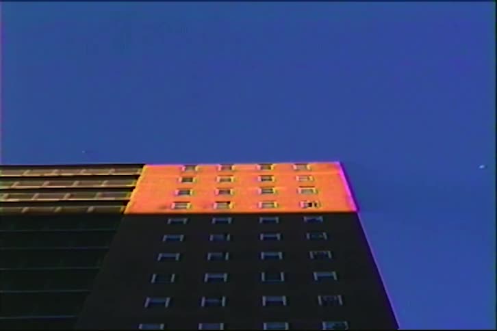 Vintage VHS footage captures the top floors of a skyscraper glowing orange in the sun against a vibrant blue sky