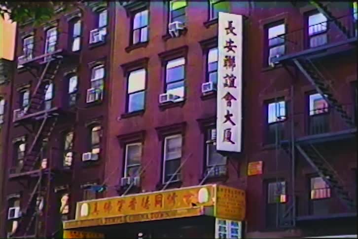 A nostalgic VHS-style shot of a classic red brick building with Chinese signage in an urban Chinatown neighborhood