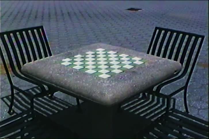 A vintage shot of a stone chessboard table with two empty chairs in an outdoor park