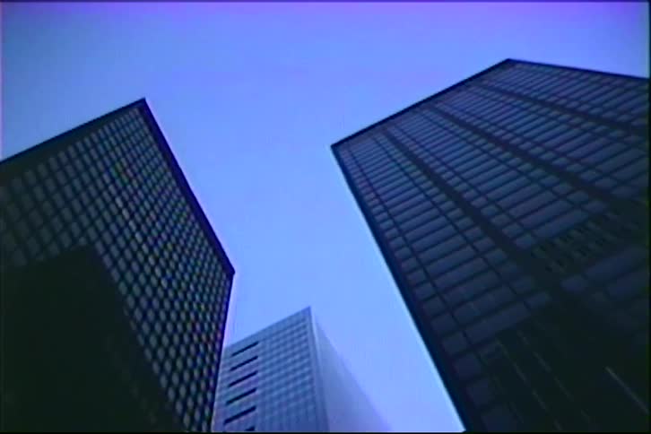 A low-angle tilt down shot of city skyscrapers against the evening sky on vintage 1980s VHS tape