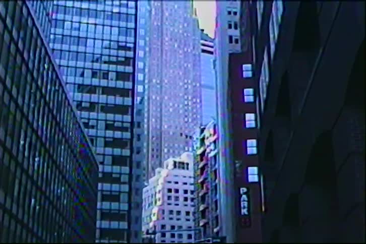 A vintage VHS-style slow upward tilt shot reveals the towering architecture of city skyscrapers