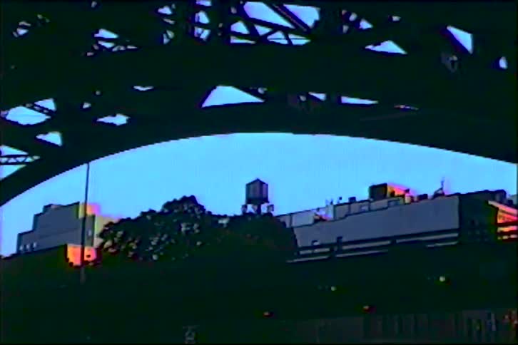 Vintage home movie footage from under a bridge slowly zooms in on a classic New York City water tower at dusk