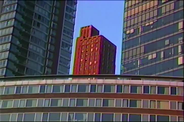 A retro VHS shot zooms out to reveal a classic red brick building framed between two modern glass skyscrapers in a downtown city