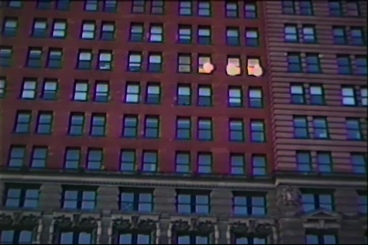 A vintage low-angle shot zooms in on the lit windows of a classic red brick urban apartment building at dusk