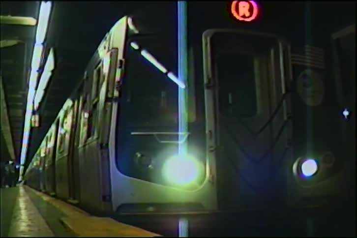Vintage VHS-style footage of a subway train with bright headlights arriving at a dark underground station at night