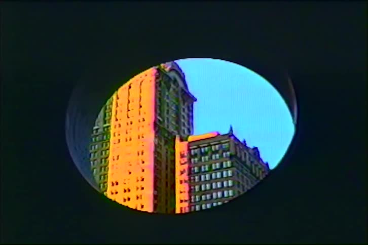 A classic skyscraper glowing in golden hour sunlight is revealed through a circular peephole in this vintage clip