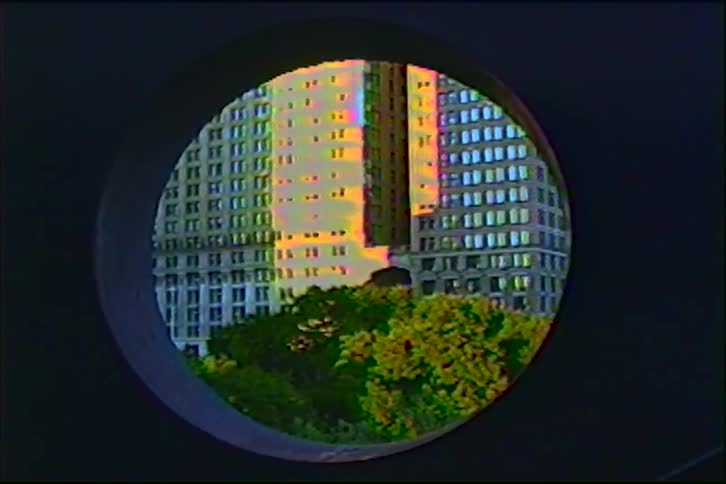 An artistic zoom-out reveals a sun-drenched skyscraper and lush green trees framed within a dark circular window