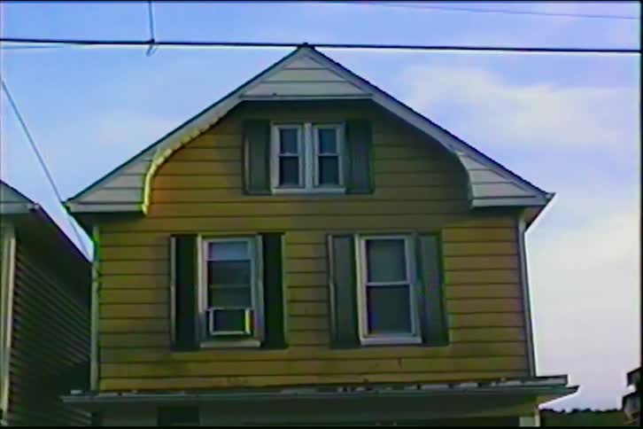 A vintage VHS shot pans across two-story suburban homes with gambrel roofs on a sunny day