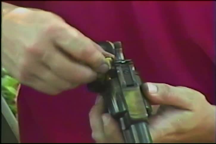 Vintage home movie footage shows a person's hands carefully loading bullets into the cylinder of a revolver