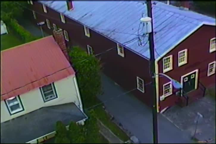 A high-angle vintage shot captures the stillness of a small town street with a large red barn and a neighboring house