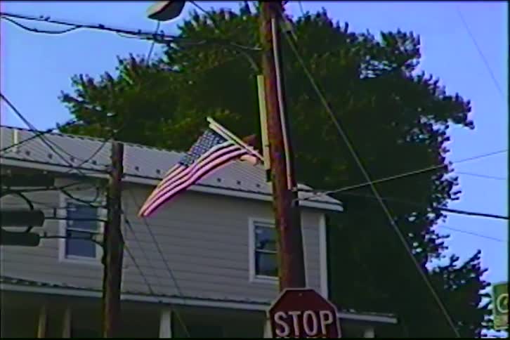 Vintage VHS footage slowly zooms in on an American flag on a utility pole in a quiet, small American town