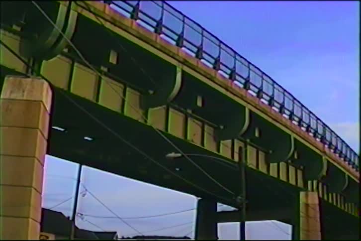 A slow camera tilt up from a quiet neighborhood street reveals the large structure of an overpass in this vintage VHS footage