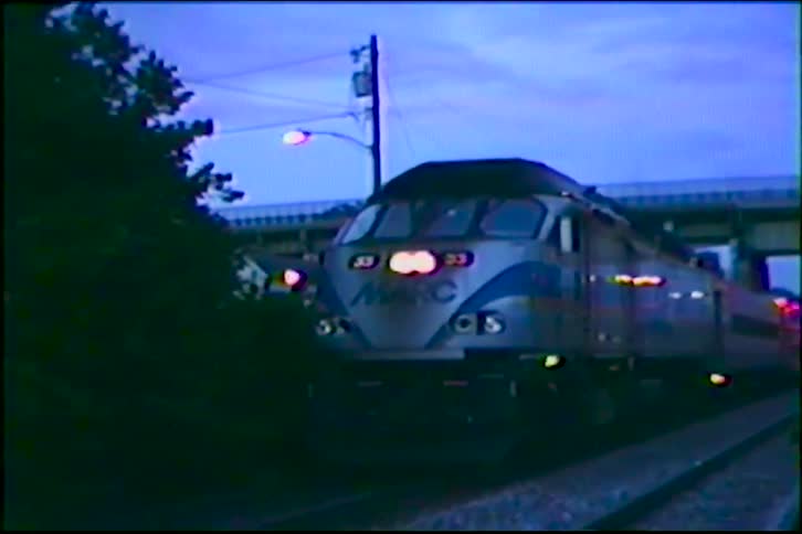 A MARC commuter train with its headlights on approaches on the tracks at dusk in this grainy vintage footage