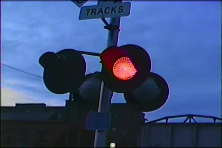 Vintage VHS footage shows a railroad crossing signal with flashing red lights as a train passes at dusk