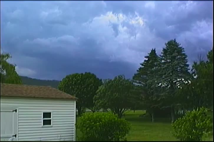 Lightning flashes within dark storm clouds gathering over a peaceful backyard with a white shed