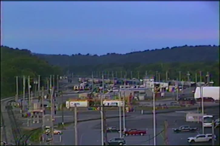 Vintage VHS footage slowly zooms in on a sprawling industrial complex and rail yard nestled in a valley at twilight