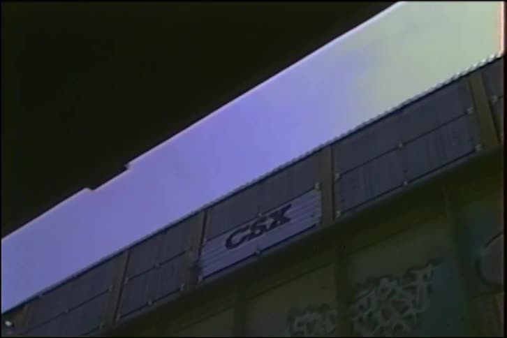 A low-angle view from under an overpass captures a graffiti-covered CSX freight train moving along an elevated track