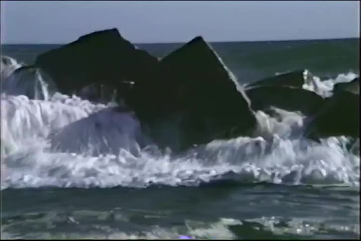 A powerful ocean wave crashes over a rocky breakwater in dramatic slow-motion vintage footage
