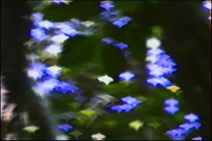 Vintage footage of abstract star-shaped blue and white bokeh lights shimmering against a dark, blurry background