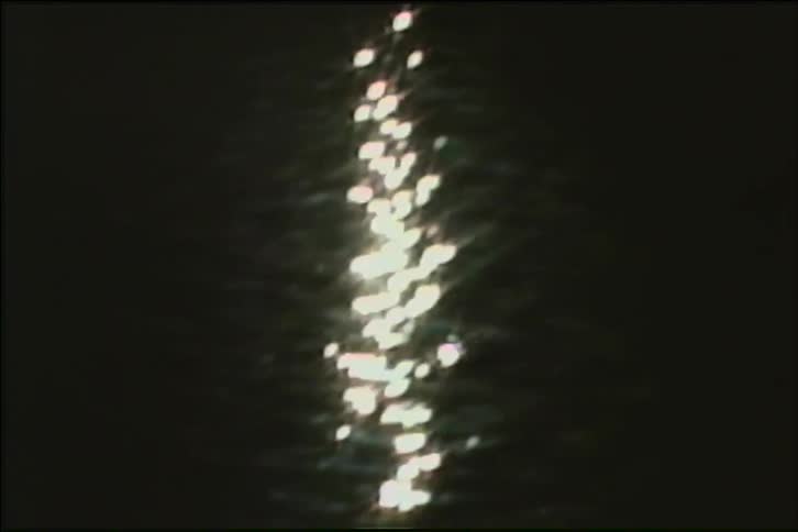 A shimmering column of light reflects and sparkles on the surface of dark, rippling water at night