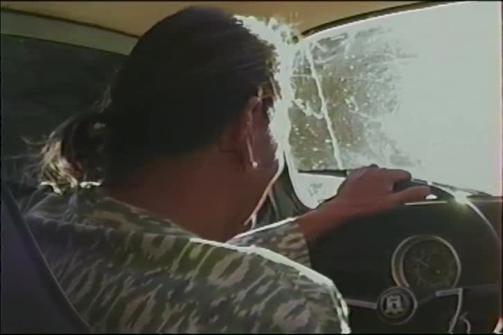 A woman with a ponytail smiles while driving a vintage car down a country road during a hazy golden hour sunset