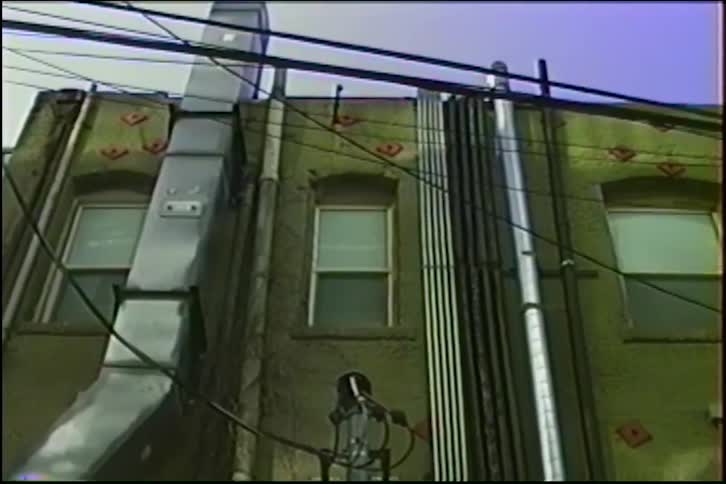 A slow zoom into a single window on the back of an industrial urban building covered in pipes and wires