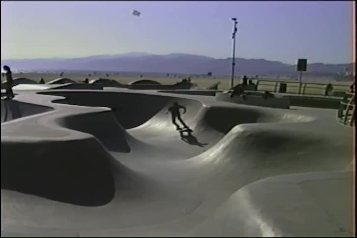 Vintage VHS footage shows skateboarders cruising through the concrete bowls of the Venice Beach skatepark on a sunny day