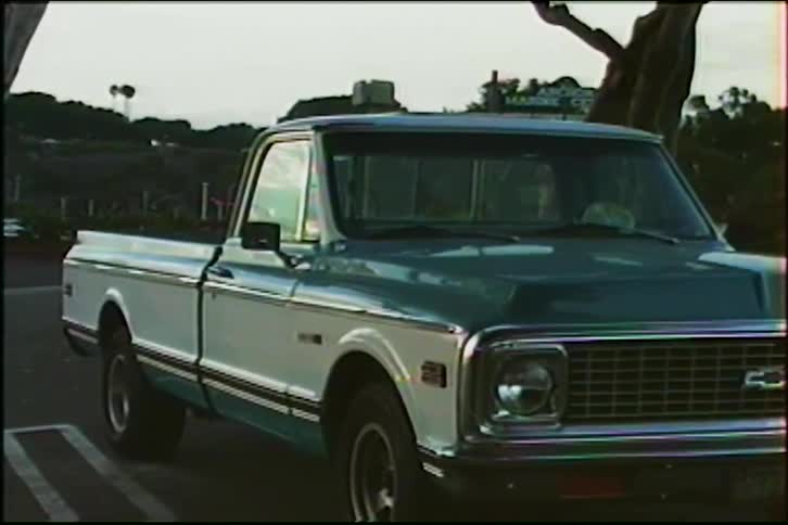 A static shot of a vintage green and white Chevrolet pickup truck from the 1970s parked in a lot