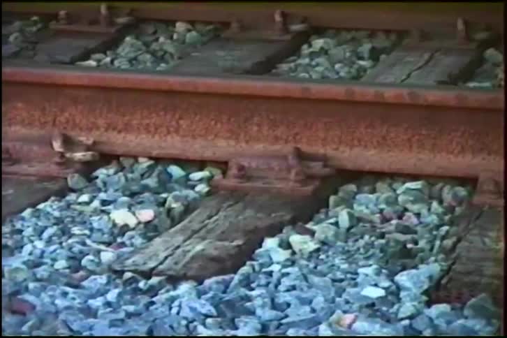Vintage home video footage shows a close-up of a rusty railroad track as a train quickly passes by