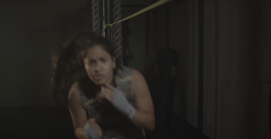 A woman is shadow boxing in a dark gym