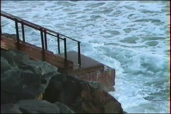 Vintage slow-motion footage shows powerful waves crashing against a rocky pier and stairs