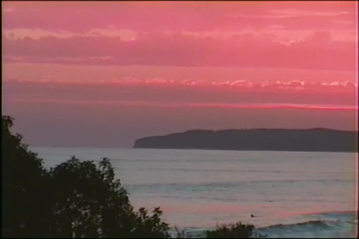 A stunning pink and red sunset illuminates the clouds over the ocean in this vintage VHS-style footage