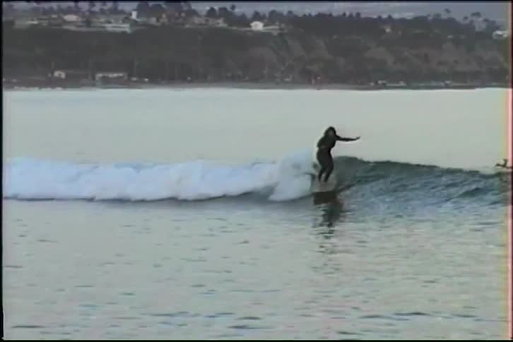 Vintage VHS footage of a woman with long hair skillfully surfing a gentle wave on a longboard