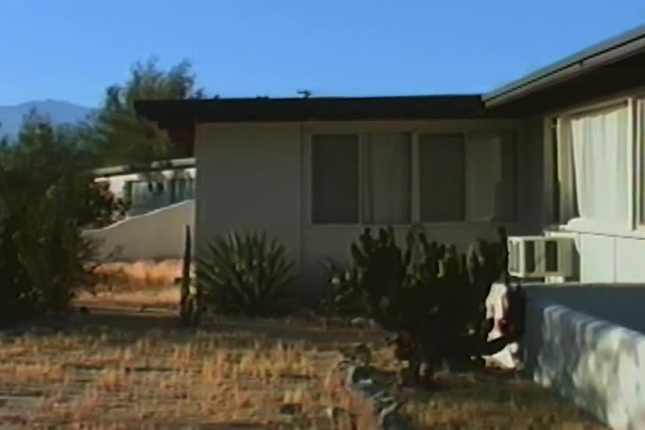 A vintage VHS shot of a mid-century modern home with a desert-scaped yard