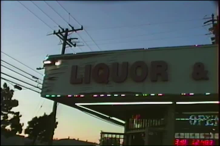 A vintage VHS-style shot captures a weathered liquor store sign against the twilight sky