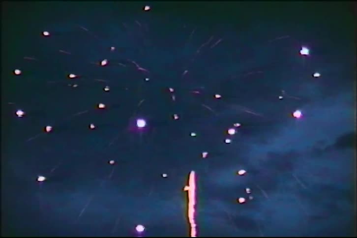 A vintage 8mm film captures a colorful fireworks display exploding against a dark night sky