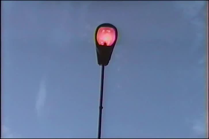 A streetlight flickers on with a reddish glow against a dimming sky in a vintage slow zoom shot