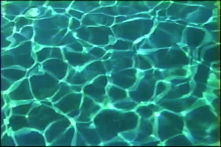 Hypnotic patterns of sunlight reflect and ripple on the surface of a green-blue swimming pool