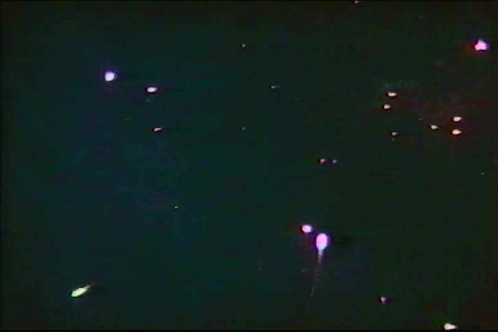 A series of colorful fireworks explode in the night sky in this grainy, vintage VHS footage